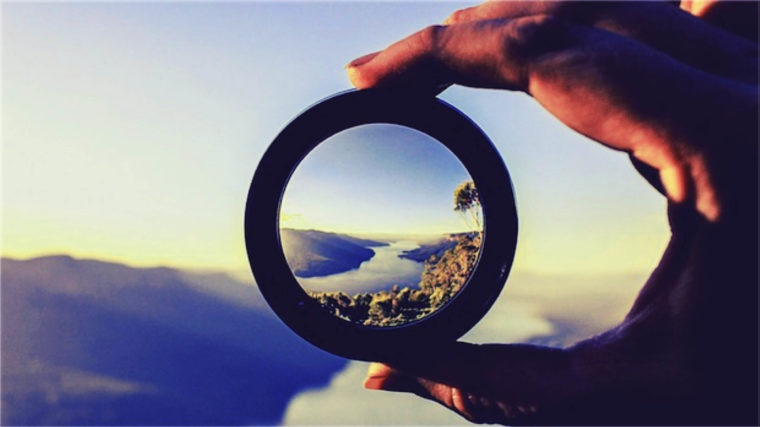 Image of a hand holding a lens, with the center in focus, to capture the concept of vision.