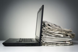 Photo of a laptop next to newspapers.