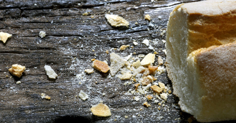 A photo of breadcrumbs on a table near a loaf of bread that has been cut. 