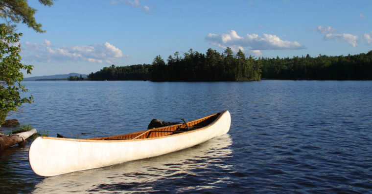 This is a photo of a canoe on a beautiful river in Maine with a blue sky above. 