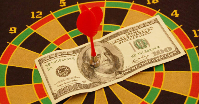 Dartboard with a magnetic dart on a one-hundred dollar bill. 